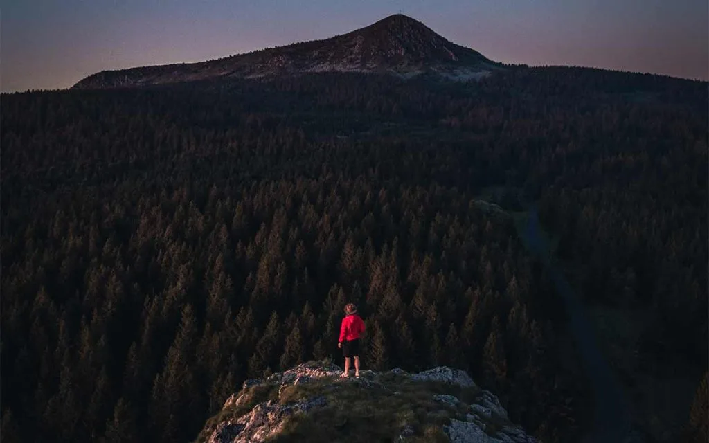 Een persoon bovenop een rots die het bos en de Mont Mézenc in Haute-Loire, Auvergne overweegt
