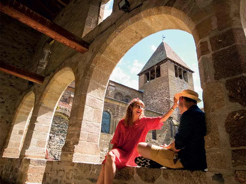 Un couple assis sur un muret sous une arche rit ensemble en Haute-Loire, Auvergne
