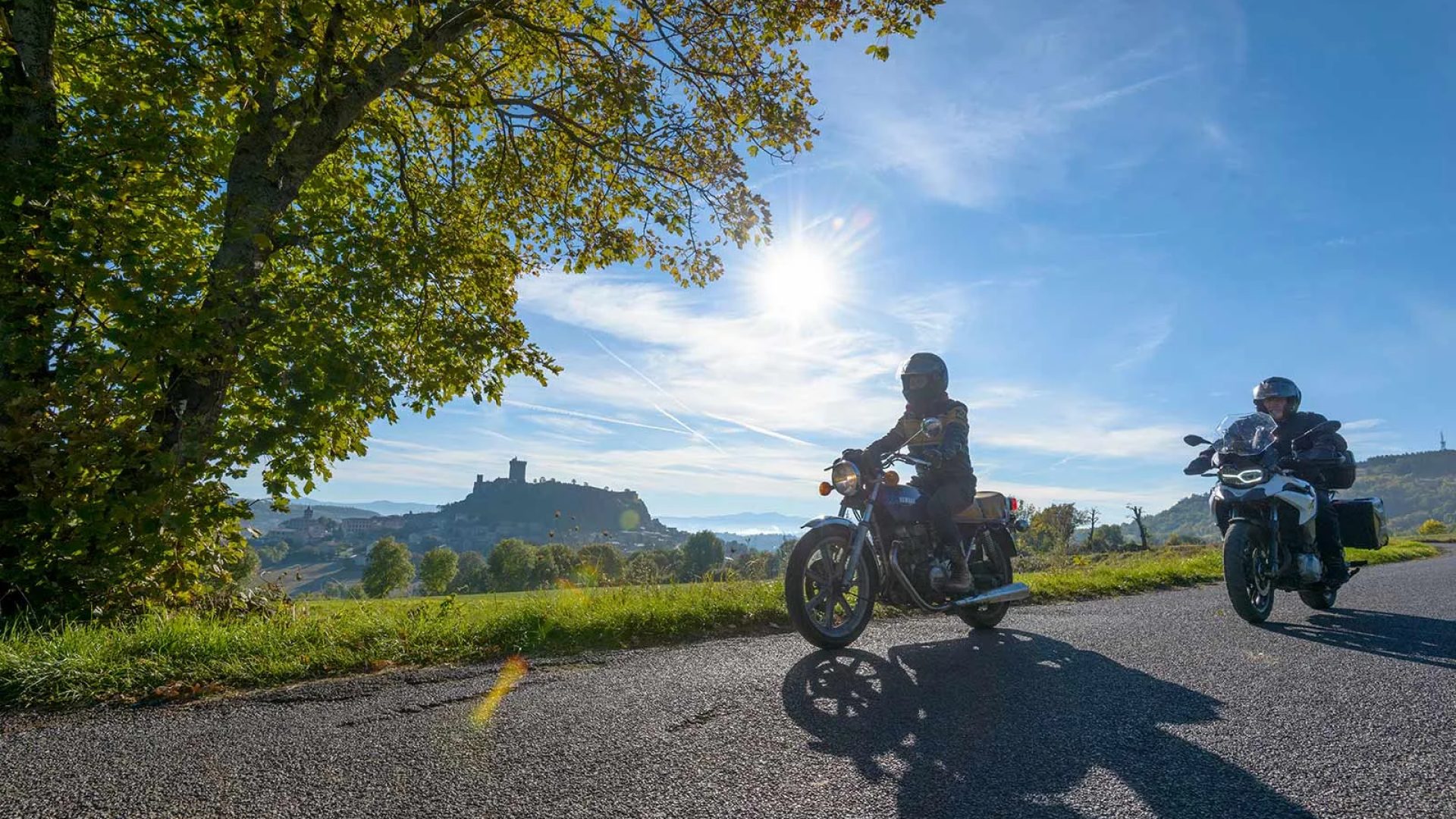 Two bikers on the road with a view of the fortress of Polignac in Haute-Loire