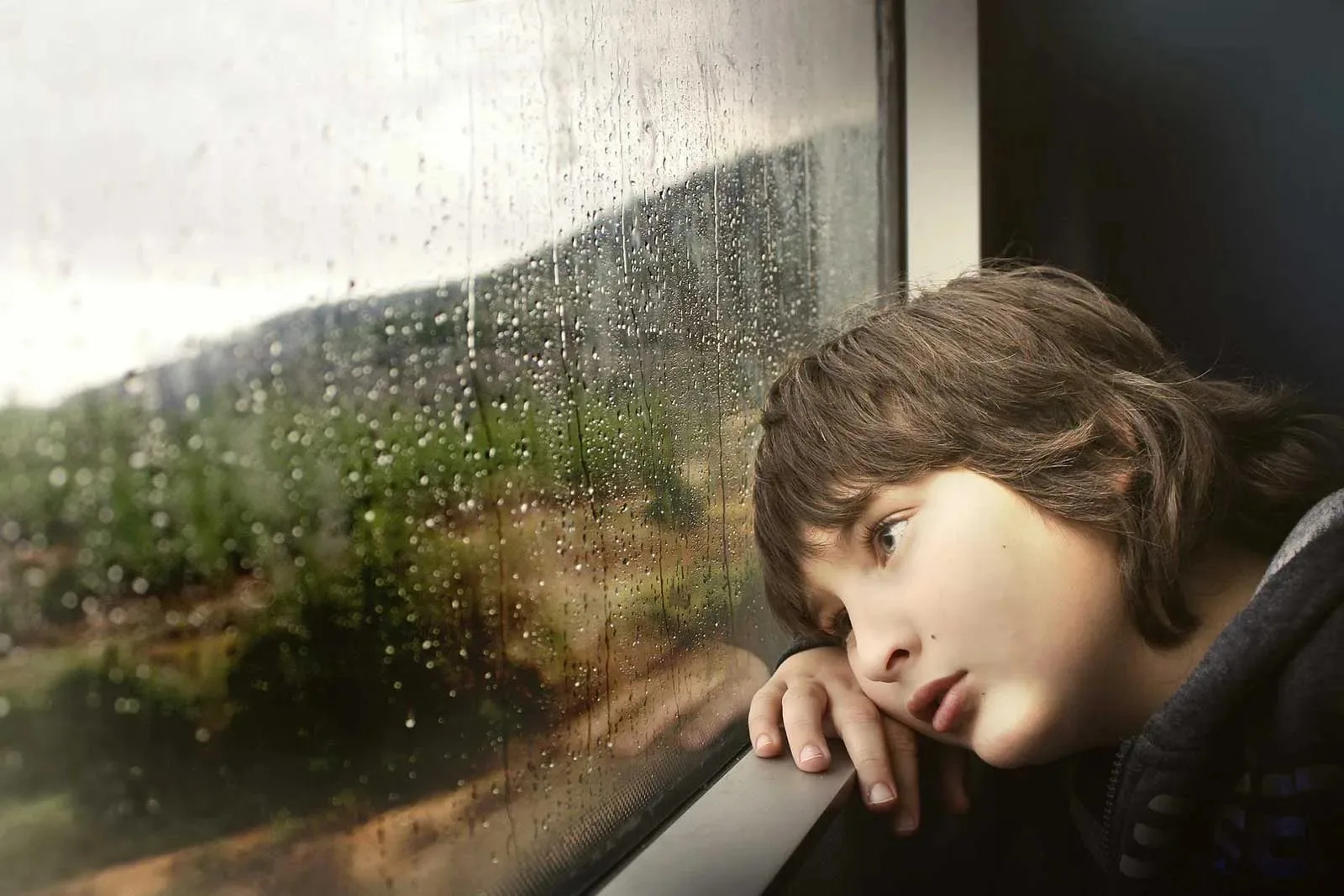Un enfant regarde dehors à travers la vitre parsemée de pluie du train en Haute-Loire