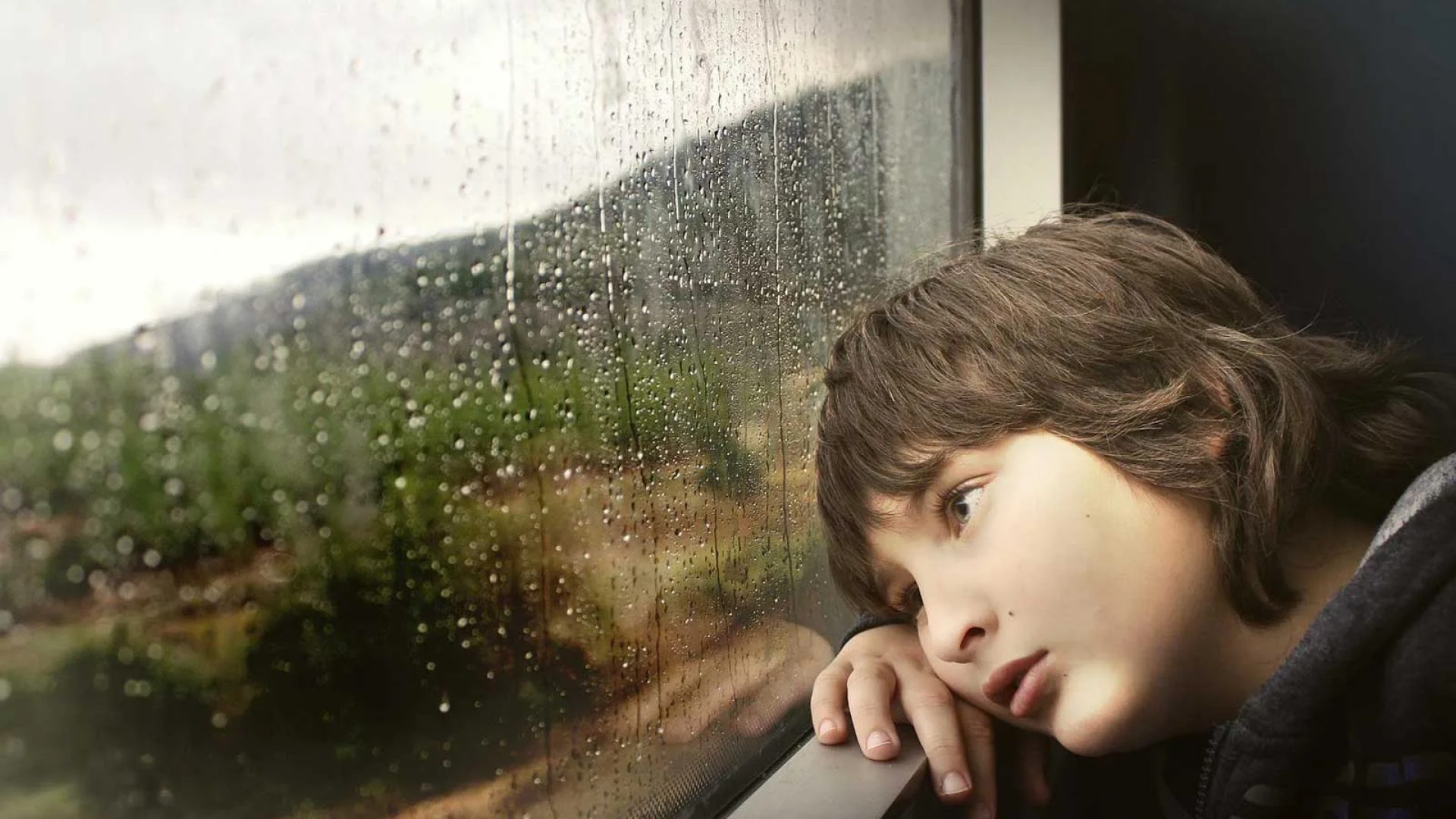 Un bambino guarda fuori dal finestrino del treno cosparso di pioggia nell'Alta Loira