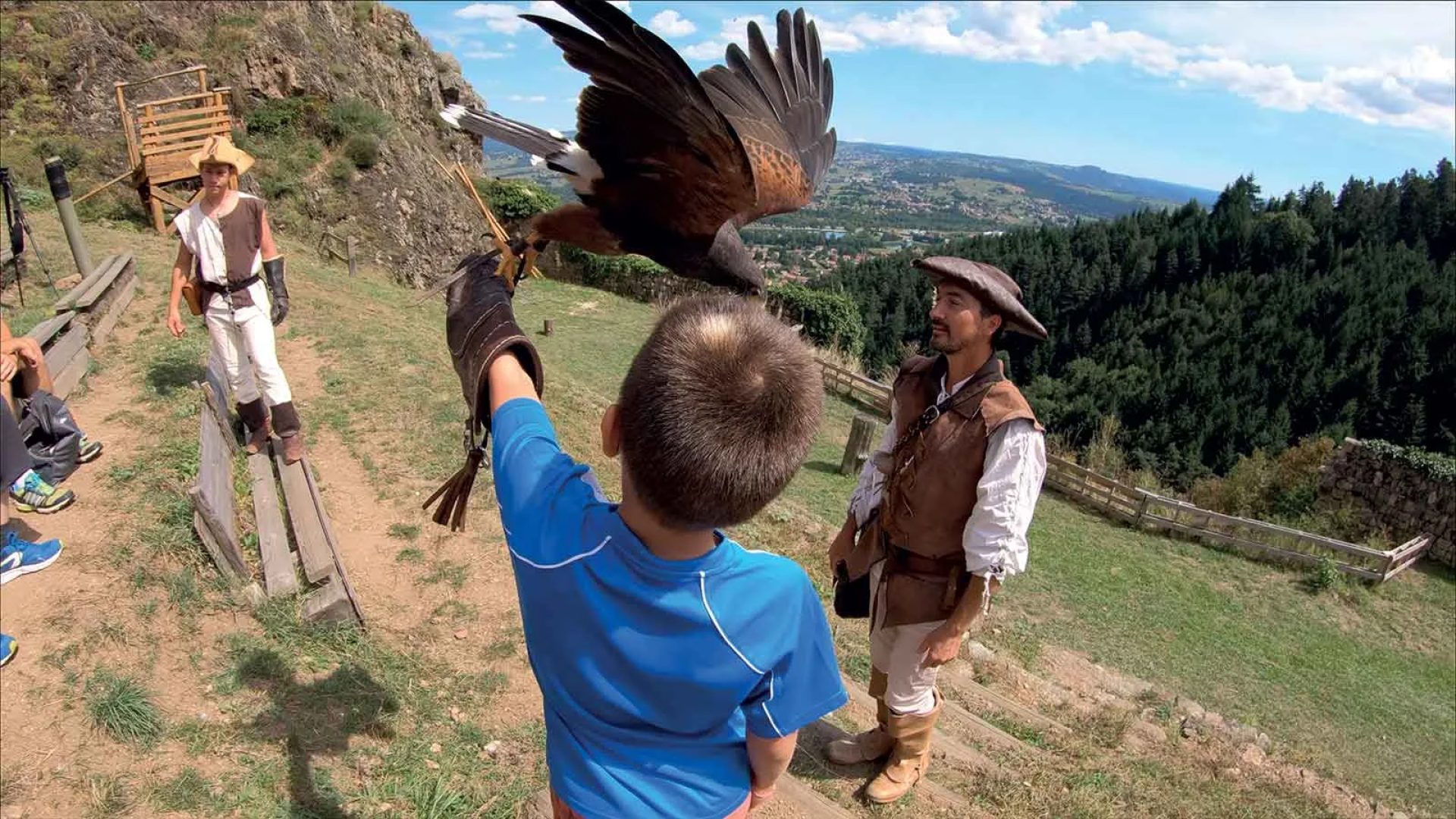A boy lands a falcon on his arm with the help of falconers in Haute-Loire