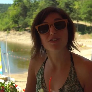 Eine Frau mit Sonnenbrille trinkt einen Drink am Strand des Lake Lavalette in Haute-Loire, Auvergne