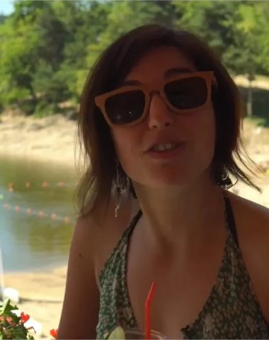 Een vrouw met zonnebril drinkt een drankje op het strand van Lake Lavalette in Haute-Loire, Auvergne