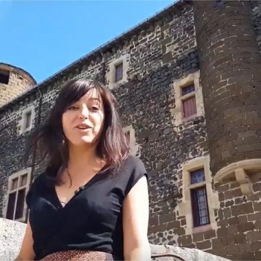 Una mujer sonriente habla frente a un castillo en Alto Loira, Auvernia