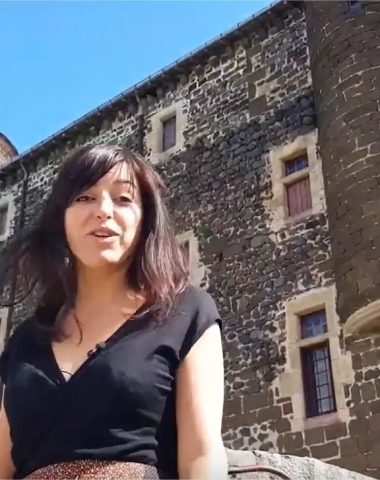 Una mujer sonriente habla frente a un castillo en Alto Loira, Auvernia
