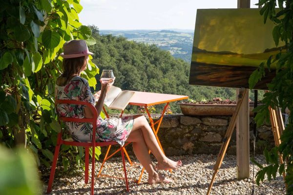 Eine Frau liest mit einem Glas in der Hand und betrachtet die Aussicht in Haute-Loire, Auvergne