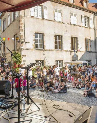 Un cantante actúa en un escenario al aire libre frente a una multitud de personas sentadas en el Apéros musique de Blesle en Haute-Loire, Auvernia.