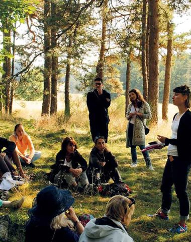 Un gruppo di persone si siede nella foresta e ascolta una donna che conta una storia per le Conferenze sotto l'albero in Haute-Loire, Alvernia