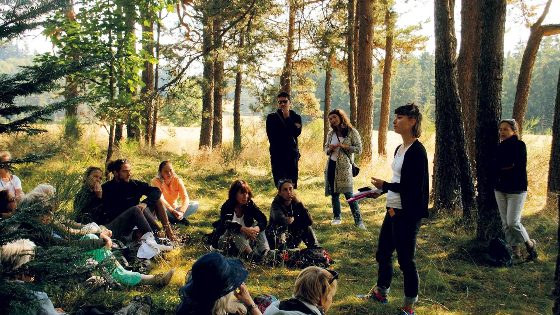 Un grupo de personas se sientan en el bosque y escuchan a una mujer contar una historia para las conferencias bajo el árbol en Haute-Loire, Auvergne