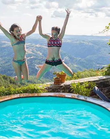 Young girls jump into a swimming pool with a view of the valley in Haute-Loire, Auvergne