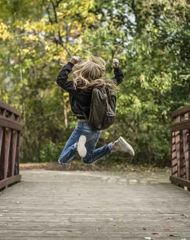 Ein Mädchen mit Rucksack hüpft vor Freude auf einer Brücke in Haute-Loire, Auvergne