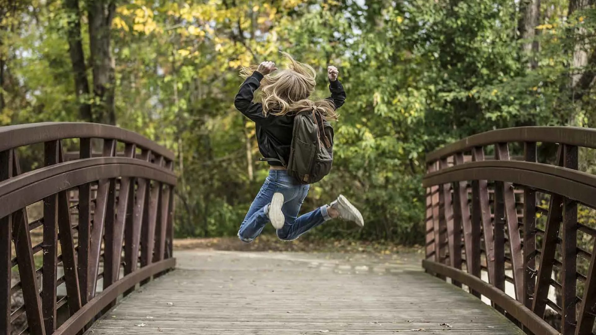 Een meisje met een rugzak springt van vreugde op een brug in Haute-Loire, Auvergne