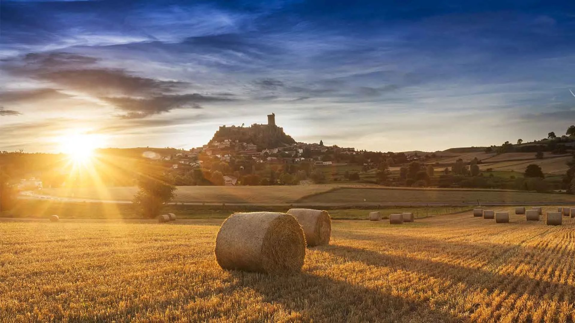 Een ondergaande zon boven een veld met op de achtergrond het fort van Polignac in de Haute-Loire, Auvergne