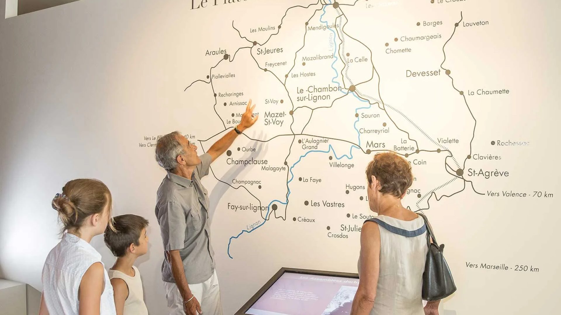 Eine Familie betrachtet die Karte der Hochebene Vivarais Lignon an einer Wand des Gedenkortes in Chambon-sur-Lignon in Haute-Loire, Auvergne
