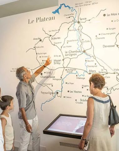 Eine Familie betrachtet die Karte der Hochebene Vivarais Lignon an einer Wand des Gedenkortes in Chambon-sur-Lignon in Haute-Loire, Auvergne