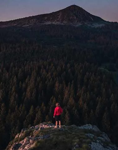 Een persoon bovenop een rots die het bos en de Mont Mézenc in Haute-Loire, Auvergne overweegt