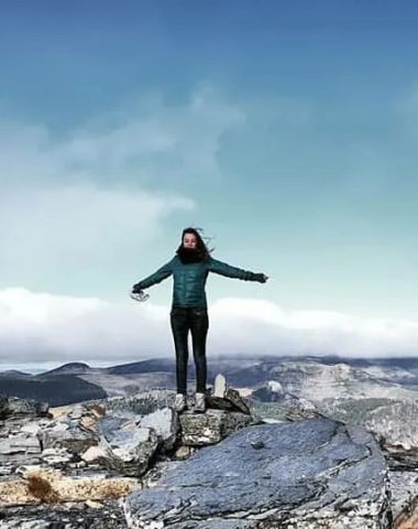 A woman with arms outstretched to the sides breathing in the fresh air of the Loire gorges at the top of Mont Gerbier in Haute-Loire, Auvergne