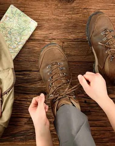 Persona atando sus zapatos para caminar junto a su mochila y su mapa de Alto Loira, Auvernia