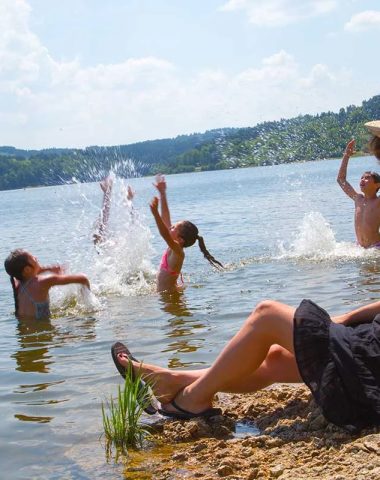 Een vrouw die hard op de oever zit, kijkt hoe haar kinderen spelen in het meer van Lavalette in de Haute-Loire, Auvergne